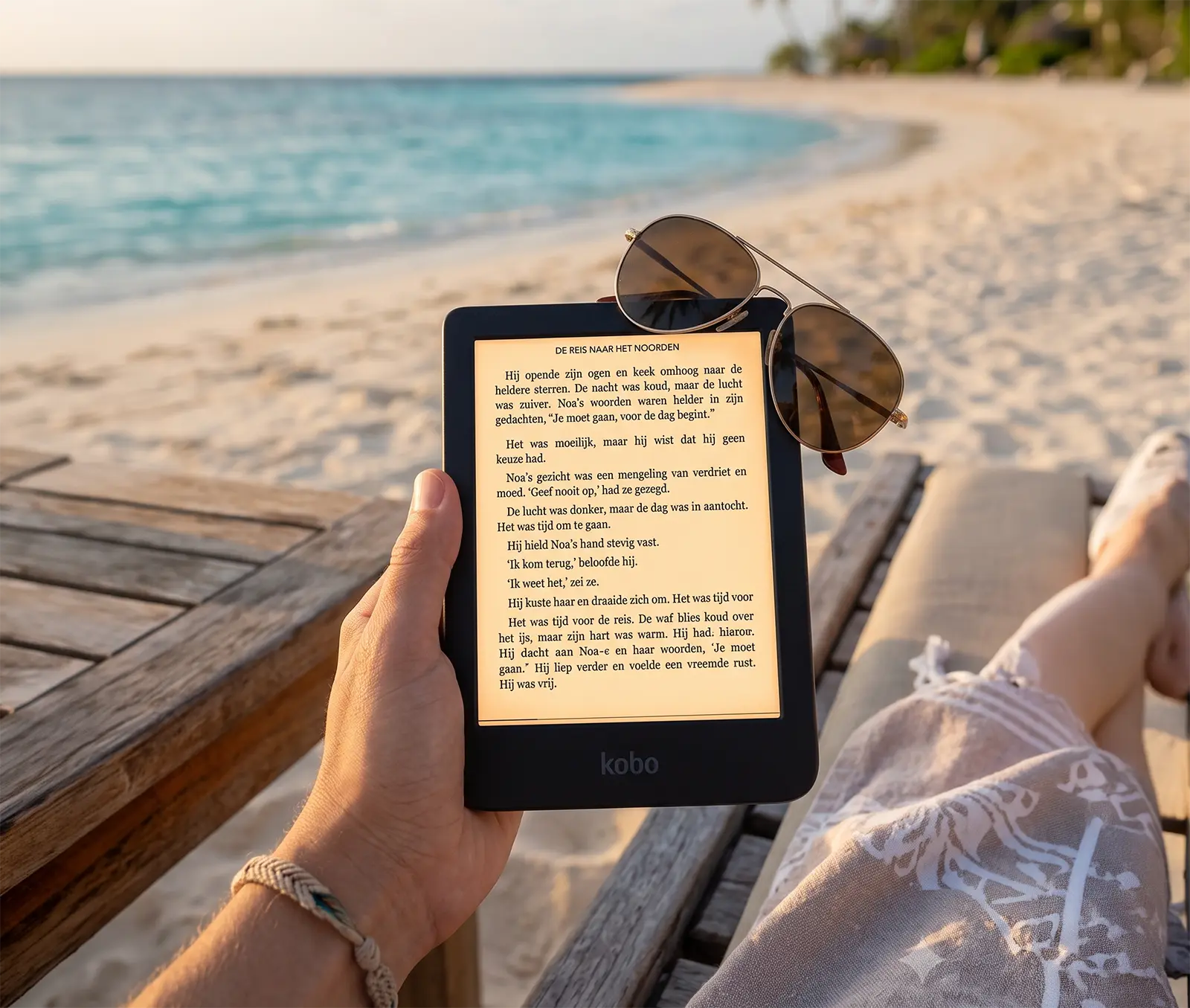 Kobo Clara BW e-reader met leesbaar e-inkscherm in fel zonlicht op het strand, zonnebril ernaast